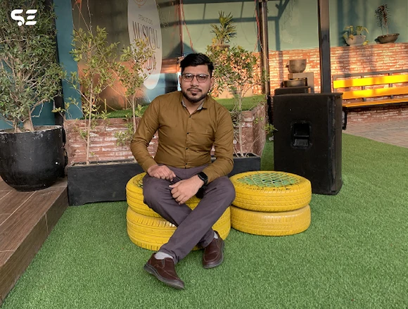 Soft Enterprise team member posing on a yellow chair during the Hi-Tea Gathering event, with a relaxed and casual atmosphere.