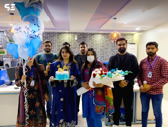 Team members posing together with a birthday cake at office celebration