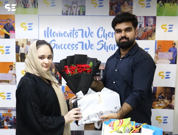 Woman in hijab receiving a gift bouquet from a masked colleague