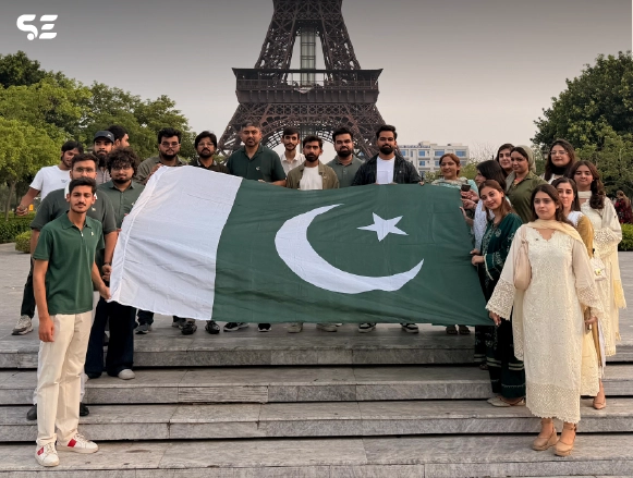Team members holding a large Pakistani flag in front of Eiffel Tower structure