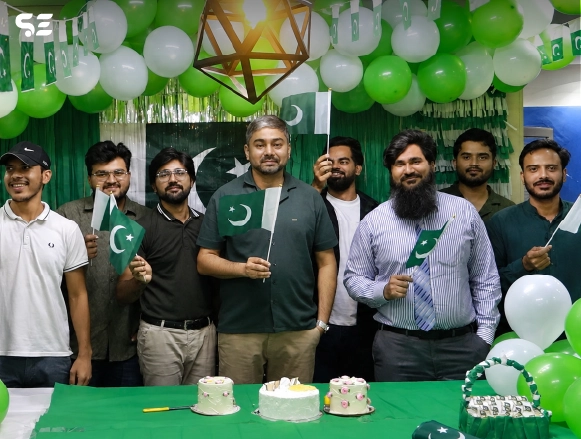 Group of colleagues posing together in front of Pakistani flag backdrop