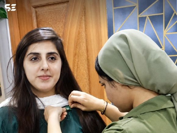 Two female colleagues adjusting a green ribbon accessory