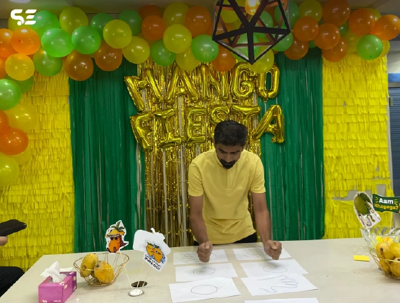 Male employee writing on paper in front of golden Mango Fiesta balloon decor
