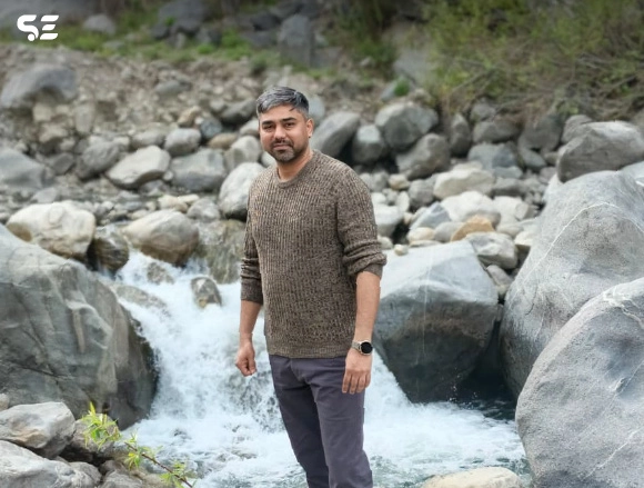 Male employee standing near a rocky stream in mountainous terrain