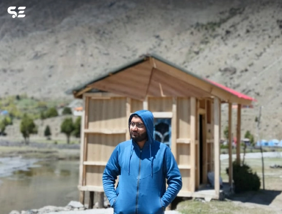 Male employee standing near a wooden cabin in a mountain valley