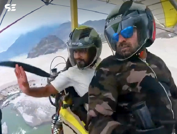 Man flying a powered paraglider over mountain terrain