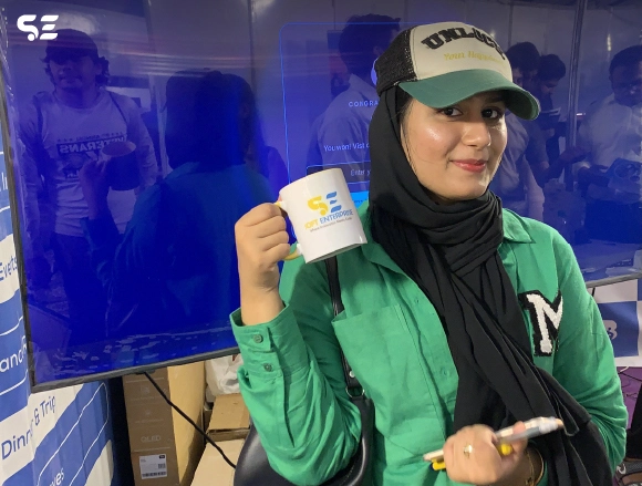 Female employee in green hoodie smiling while holding a mug